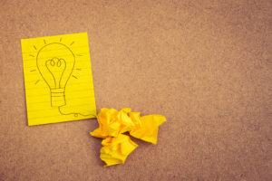 Hand writing light bulb on yellow paper on brown background with crumpled paper ball - business concept idea and strategy